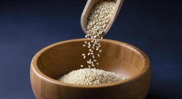 White Sesame Seeds Pouring from a Wooden Scoop into a Polished Wooden Bowl photo