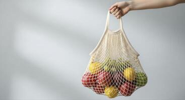 Hand holding a beige woven mesh grocery bag filled with fresh fruit for eco friendly shopping photo