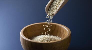 White Sesame Seeds Pouring from Wooden Scoop into Bowl for Healthy Cooking and Baking photo
