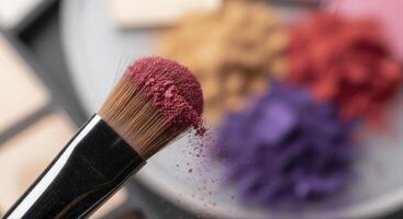 Close up of a makeup brush with pink powder and blurred colorful cosmetic products photo