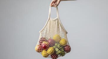 Hand holding a reusable mesh grocery bag filled with fresh apples and lemons photo