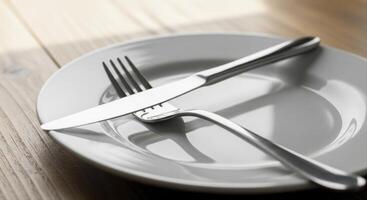 White ceramic plate with polished silver fork and knife on a light wooden table photo