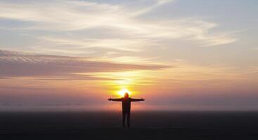 Man with outstretched arms silhouetted against a vibrant sunset sky photo