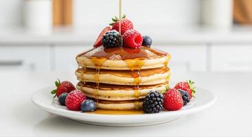 Golden pancakes stacked on a white plate with maple syrup and fresh mixed berries photo
