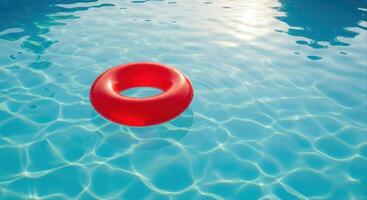 Red swimming ring float gently drifting on clear blue pool water with sunlight reflections photo
