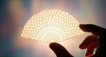 Hand holding a delicate translucent fan shaped wafer with intricate geometric pattern photo
