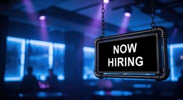 Now Hiring sign illuminated in a dark bar or club with blue and purple lights photo