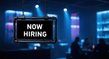 Now Hiring sign hanging in a dimly lit bar or club, indicating job openings. photo