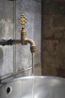 Water flowing from an old brass faucet in a rustic setting photo