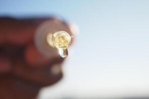 A person holds a dropper tube with aessential oil drop glistening in sunlight photo