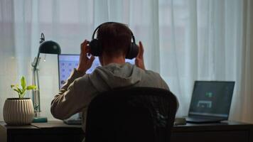 Man working at desk with two screens and headphones, back view. Focused freelancer editing digital content in modern home office setup video