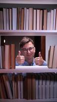 A man with glasses and a book in front of a shelf of books video