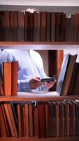 A man is looking at his phone while standing in front of a book shelf video