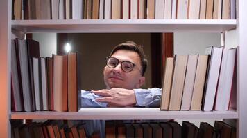 A man in glasses is leaning on a bookshelf video