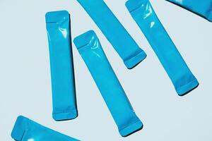Blue Foil Sachets are Scattered on Light Blue Background. Packaging for Single Serving Products. Food and Beverage Industry. photo