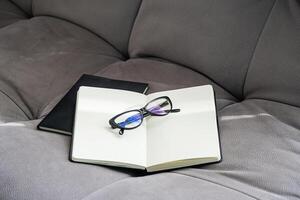 Open Notebook with Blank Pages and Pair of Glasses Rests on a Gray Couch. photo
