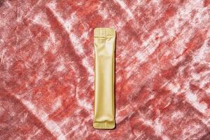 Golden Foil Stick Pack. Single Dose Sachet for Medicine, Food. Mockup Design for Brand Presentation on Velvet Surface. photo