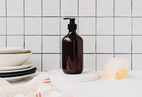 Bottle with dish detergent on marble podium with clean plates and sponge with foam photo
