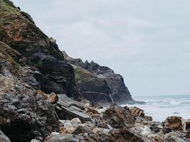 Beautiful view of a wild stone beach and oceanic waves with splashes hitting the shore photo