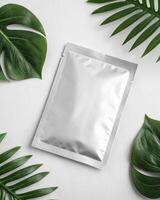 A white packet of face mask on a white table with green leaves photo
