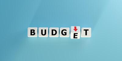 Blocks spell BUDGET with a red downward arrow. Symbolizes budget cuts, financial decrease, expense reduction, or economic challenges. Ideal for finance, accounting, cost management and crisis concepts photo