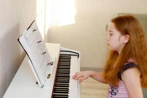 kid girl sits at the piano looking at the notes and plays the melody with her right hand. photo
