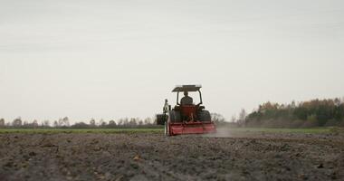 Young male farmer plows a field on a small farm tractor with a plow on an autumn day. Preparing the soil for planting winter crops photo