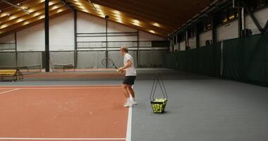 Handsome man of European appearance with an athletic build, throws tennis balls with a racket over the net one by one, taking them from a basket standing nearby, playing alone photo