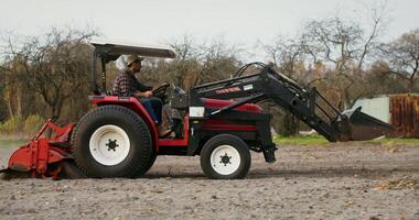 Young male tractor driver drives a modern multipurpose agricultural machine plowing a field on an autumn day. Side videography photo