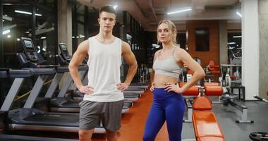 Young handsome man and woman look directly into the camera, putting their hands on the belt, standing in a modern gym without people photo