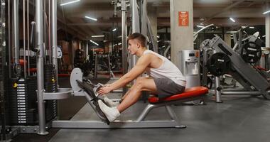 A young man, athletic physique is engaged in the gymnasium, doing exercises to look at the muscles of the chest on a modern simulator. Side videography photo