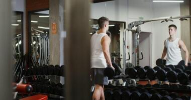 A man of European appearance, athletic physique starts workshop for biceps in a modern gym, standing in front of a mirror and choosing dumbbells photo