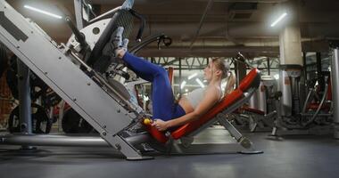 A blonde woman, dressed in sportswear, is engaged in the gym alone, doing exercises for the legs, lifting weights on the exercise machine for exercise photo