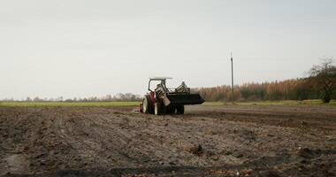 Young farmer of European appearance drives an agricultural tractor across a field on an autumn day, leaving behind even rows of plowed land photo