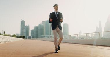 A man with glasses, wired headphones in his ears, dressed in a business suit dancing walking down the street with a mobile phone in his hands photo