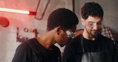Two blacksmiths of different nationalities in work clothes are considering a sketch of a future product, working together and using a tablet, close-up. 4k , red komodo photo