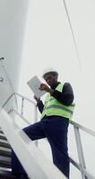 A power plant worker in work gear uses a tablet with a serious look while standing on the steps near the entrance to an industrial wind generator, vertical , bottom view. in 4k, red komodo photo
