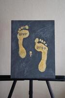 Abstract gold footprints on black canvas artwork displayed on easel in minimalist setting. photo