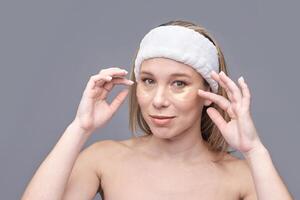 Young caucasian female applying under eye patches for skincare routine with relaxed expression. photo