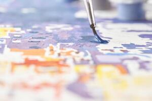 Abstract painting in progress with focus on paintbrush and colorful details on canvas. photo