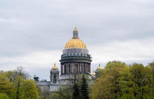 St. Isaacs Cathedral Rises Majestically With Its Golden Dome Surrounded by Lush Greenery in the Heart of St. Petersburg During Spring photo