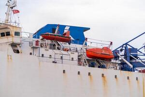 View of a cargo ship at Bosphorus with lifeboats prepared for emergency situations and colorful structures against a cloudy sky photo