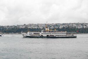 Ferry crossing the Bosphorus Strait with city skyline in background on a cloudy day photo