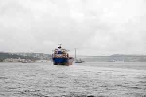 Bosphorus Strait with cargo ship navigating under cloudy skies and bridge connecting Europe and Asia in the background photo