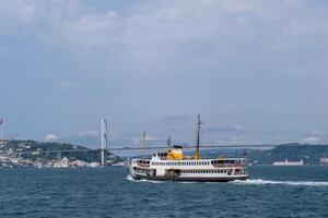 Ferry navigating the Bosphorus strait under an iconic bridge with city skyline in the background photo