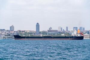 Cargo ship navigating the Bosphorus with a modern skyline in the background during a clear day photo