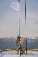 Bosphorus view from a boat with flag flying and bell in foreground on a calm and cloudy day photo