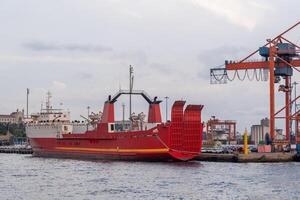 Red cargo ship docked near Bosphorus strait with cranes in the background during twilight hours photo