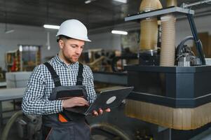 Carpenter using laptop controlling cnc machine in furniture factory photo
