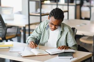 Focused university student taking notes and studying textbooks in library photo